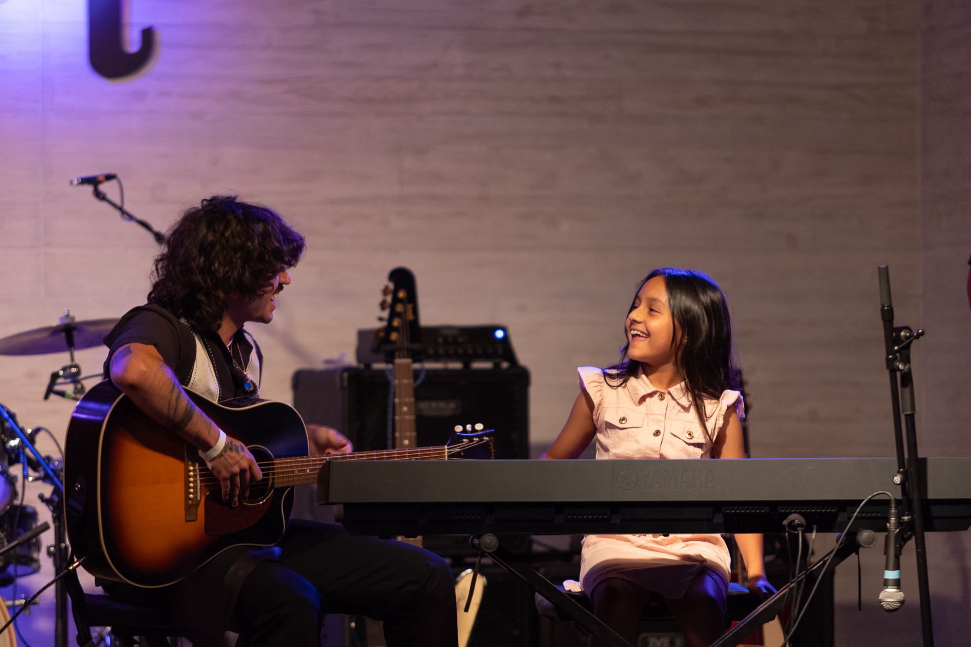 Instructor with acoustic guitar coaching a young keyboardist mid-lesson