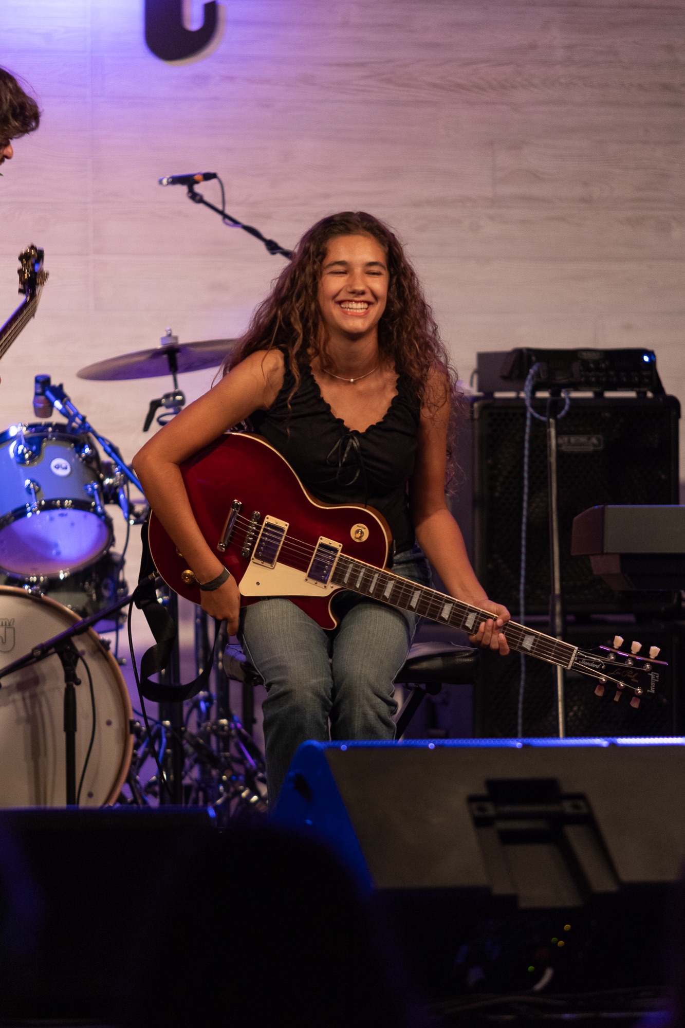 Teen camper beaming with a red electric guitar on stage